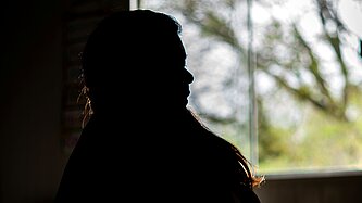 Eine Silhouette einer Frau vor einem Fenster sitzend.