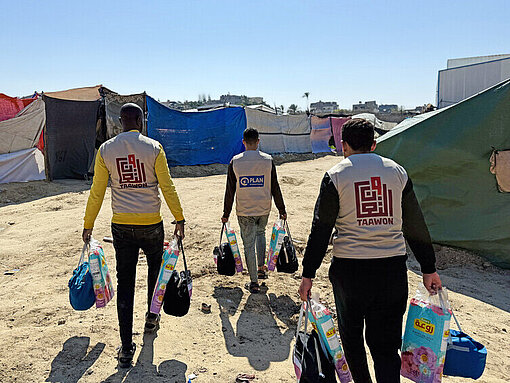Drei Plan-Mitarbeiter bringen Hygiene-Kits zu den Vertriebenen Menschen im Geflüchtetencamp in Nord-Gaza Drei Plan-Mitarbeiter bringen Hygiene-Kits in ein Geflüchtetencamp nach Nord-Gaza