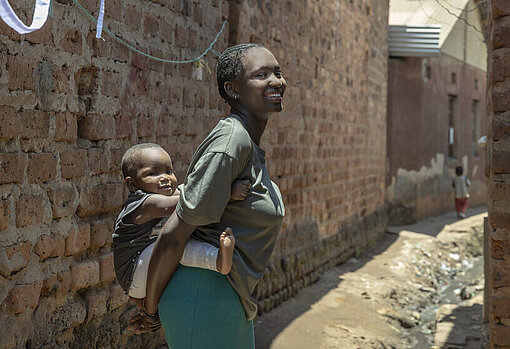 Faith trägt ihre Tochter auf ihrem Rücken in Uganda 
