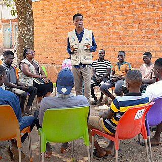 Traifon steht inmitten eines Stuhlkreises und hält eine Rede