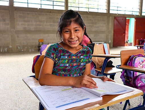 Ein Mädchen sitzt an einem Pult und liest in einem Schulbuch