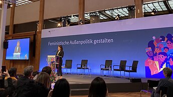 Auf dem Bild steht Ministerin Annalena Baerbock auf der Bühne und spricht zu einem Publikum. Im Hintergrund steht der Schriftzug "Feministische Außenpolitik gestalten"
