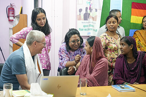 Bei ihrem Takeover spricht Sana mit dem Team des Plan-Büros in Nepal über dessen Programmarbeit Ein Mann und eine Gruppe Frauen sind an einem Konferenztisch versammelt und unterhalten sich