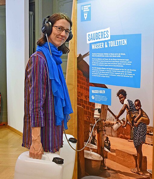 Eine Frau in bunter Bluse hebt zwei Kanister mit Wasser