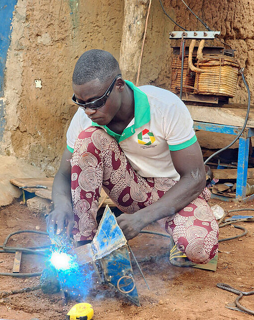 Ein Mann mit Schutzbrille hockt am Boden und schweißt Metall