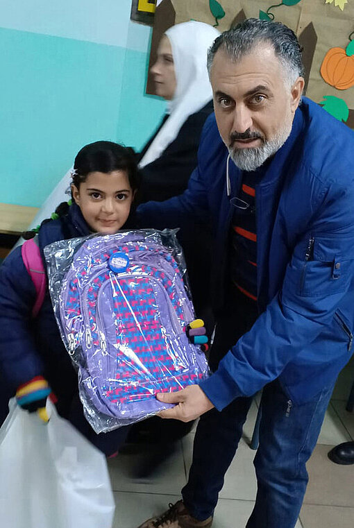 Ein Mädchen erhält von einem Plan Mitarbeiter die benötigten Schulpakete