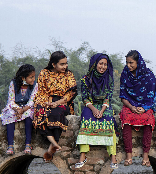 In Krisensituationen werden die Rechte von Mädchen oft zurückgestellt. Mädchen in Bangladesch sitzen auf einer Brücke und unterhalten sich.