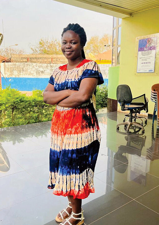Eine junge Frau aus Guinea-Bissau trägt ein buntes Kleid. Sie hat die Arme verschränkt und schaut ernst in die Kamera