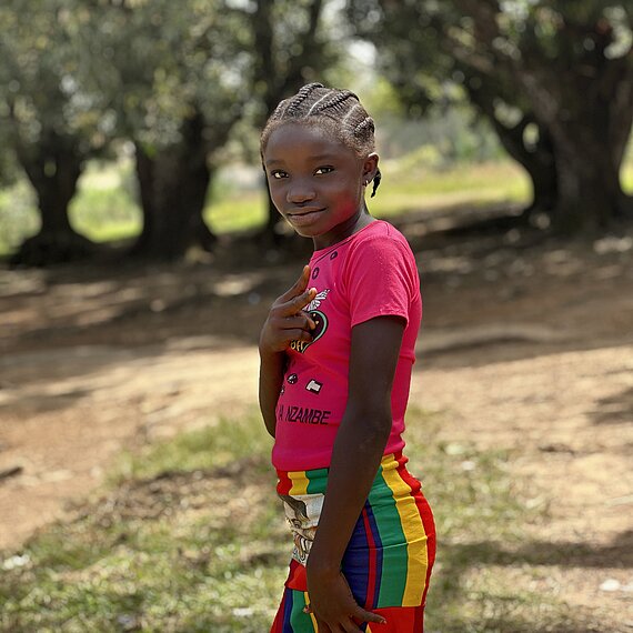 Ein Mädchen steht lächelnd vor ein paar Bäumen