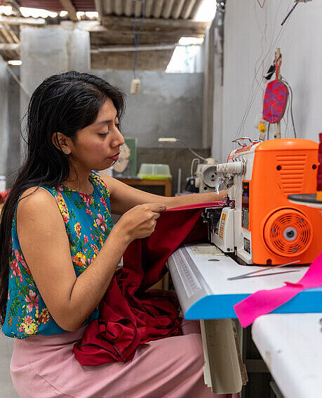 Eine junge Frau sitzt an einer Nähmaschine und arbeitet konzentriert an einem Kleidungsstück.