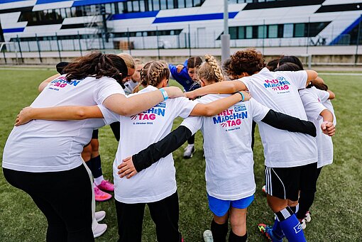 Taktik ist alles: Lagebesprechung beim Mädchenfußballtag mit dem HSV Mädchen in Fußballtrikots stehen nach vorne gebeugt im Kreis zusammen und haben sich die Arme um die Schultern gelegt