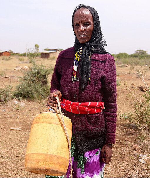 Wasserholen Eine Frau steht auf trockenem Land und hält einen Kanister für Wasser in der Hand