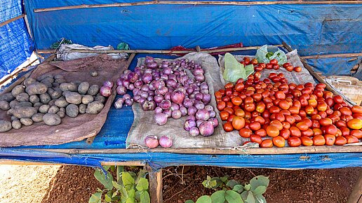 Kartoffeln, Zwiebeln und Tomaten liegen an einem Verkaufsstand aus.