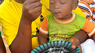 Mangelernährung stoppen Eine Frau füttert das kleine Kind, das auf ihrem Schoß sitzt.