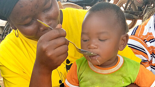 Mangelernährung stoppen Eine Frau füttert das kleine Kind, das auf ihrem Schoß sitzt.