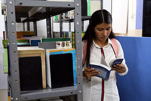 Junge Frau in weißer Bluse liest ein Buch in einer Bibliothek