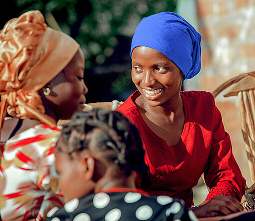 Drei Frauen in bunter Bekleidung sitzen an einem Tisch und unterhalten sich