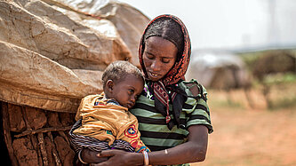 Eine Frau hält ihr Kleinkind im Arm und schaut besorgt auf es herab