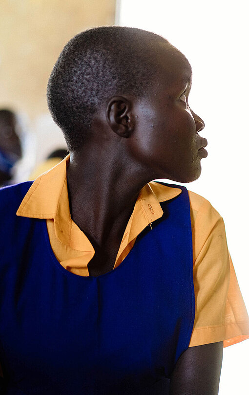 Jane hat es vermisst, als Schulsprecherin für ihre Mitschülerinnen da zu sein. Jane, eine Jugendliche in Schuluniform sitzt im Klassenraum und schaut zur Seite, sodass ihr Gesicht im Profil zu sehen ist.