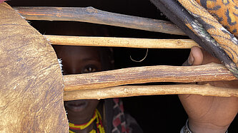 Man sieht nur schemenhaft das Gesicht eines Mädchens in einer Hütte hinter einigen Ästen