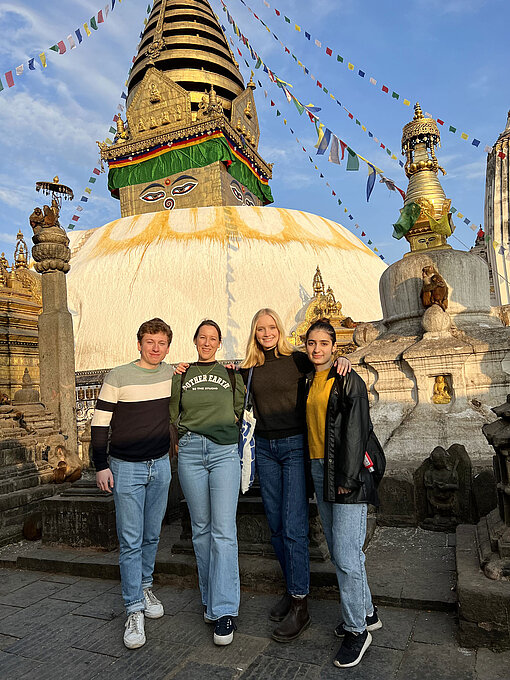 Während der Reise wurden auch nepalesische Kulturgüter besucht: Hier zum Beispiel Swayambhunath Stupa, der auch als Affentempel bekannt ist. Vier Menschen stehen vor einer Tempelanlage.
