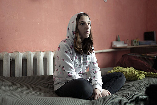 Ein 15-jähriges Mädchen im Kapuzenpulli sitzt auf einem Bett