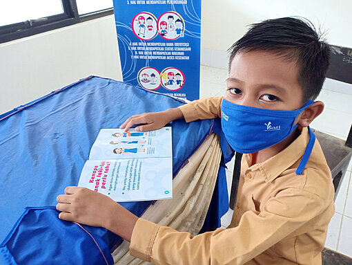 Ein Junge trägt einen Mund-Nasen-Schutz und liest in einer Broschüre