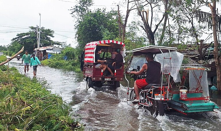 Menschen überqueren zu Fuß und in Tricycles die überfluteten Straßen in der Region MIMAROPA