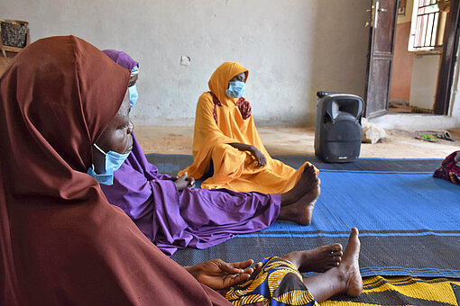Frauen in bunten Kleidern sitzen auf dem Boden eines Raumes und diskutieren