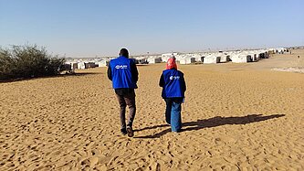 Zwei Mitarbeitende von Plan International laufen auf ein großes Geflüchtetencamp zu