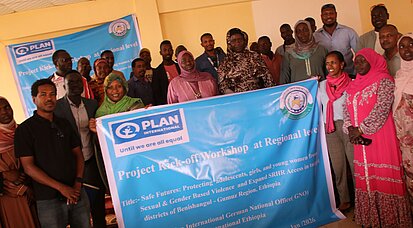 Eine Gruppe von Menschen steht in einem Raum, der als Veranstaltungsort dient, und hält ein großes Banner mit der Aufschrift „Project Kick-off Workshop at Regional level“.