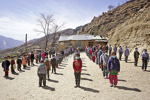 Alle Schulkinder nehmen gemeinsam an Sport-, Lern und Spielaktivitäten teil Schulkinder stehen auf einem sandigen Feld in den Bergen des Himalajas in Nepal beisammen