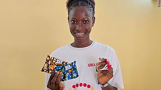 Carla steht bei einer Veranstaltung zum Menstruationsgesundheitstag und präsentiert Informationsmaterialien