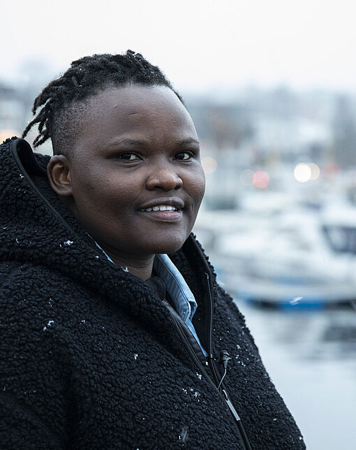 Eine Frau steht mit einer dicken Jacke draußen an einem Hafen. Es schneit.