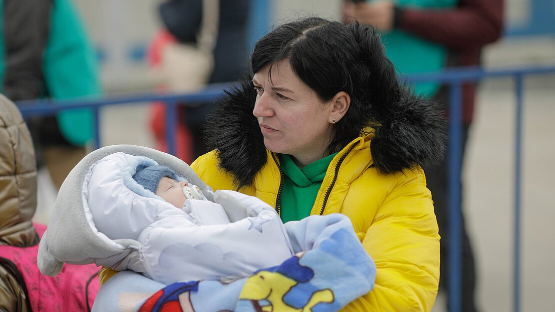 Eine Mutter mit einem Baby auf dem Arm, das in dicke Decken gewickelt ist