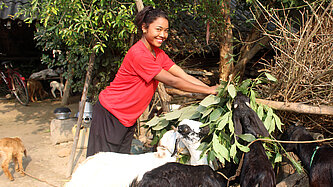 Junge Frau steht neben ein paar Ziegen und füttert sie mit Grünzeug