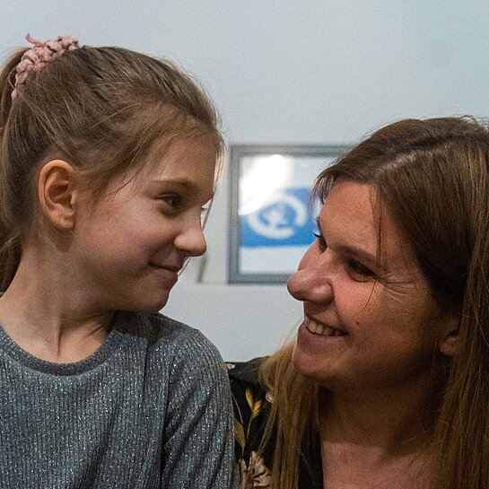 Mutter Halyna hat Tochter Zlata auf dem Schoß und sie lächeln sich an