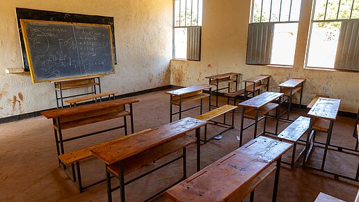 Ein leeres Klassenzimmer mit Schultischen und -bänken und einer beschriebenen Tafel