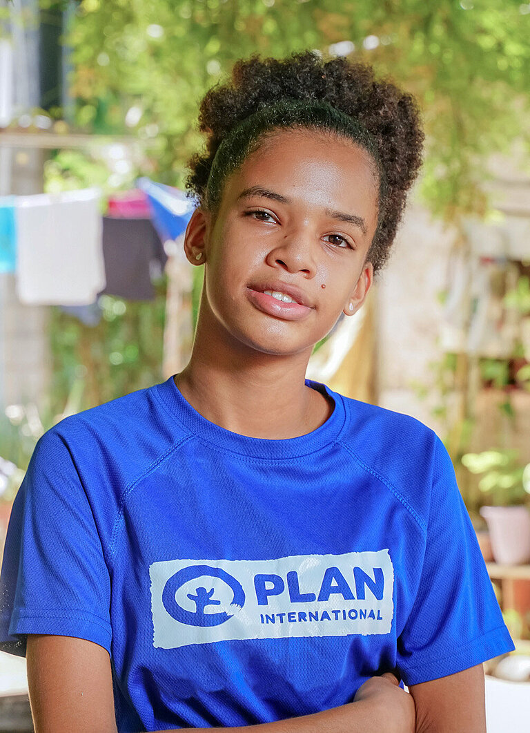 Eine junge Frau steht mit verschränkten Armen und schaut ernst in die Kamera