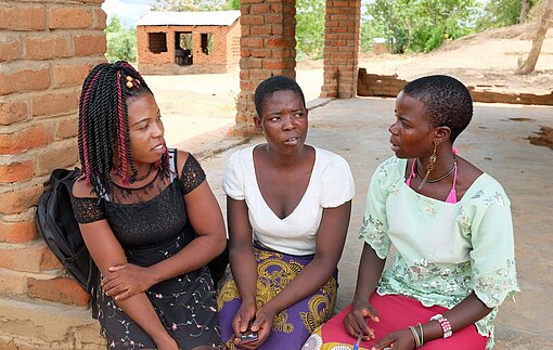 Nester spricht mit den neu ausgebildeten Sexualaufklärerinnen Angela (22) und Lyness (20, v. r.) Drei Frauen in Malawi unterhalten sich