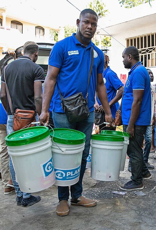 Die Teams von Plan International Haiti verteilen Eimer mit Hygieneartikeln an geflüchtete Familien Ein Mann verteilt Hygienesets