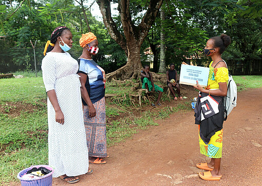 Drei Frauen stehen sich gegenüber und eine zeigt den anderen beiden Aufklärungsmaterial zu Tuberkulose