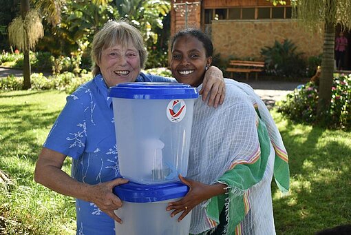 Das Wasserfiltersystem schützt Menschen vor Krankheiten und bietet ihnen einen gesicherten Zugang zu Wasser. Patin und Frau mit einem Wasserfilter.