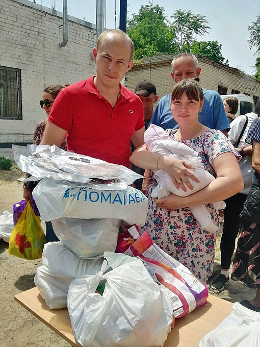 Die ukrainische Hilfsorganisation Pomogaem, ein Partner von Plan International, verteilt Nothilfepakete an Familien im Katastrophengebiet Menschen stehen an einem Tisch mit Hilfsgütern