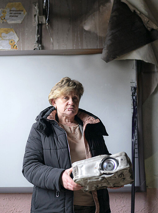 Eine Frau hält einen kaputten Projektor in der Hand, dessen Plastikhülle geschmolzen ist.