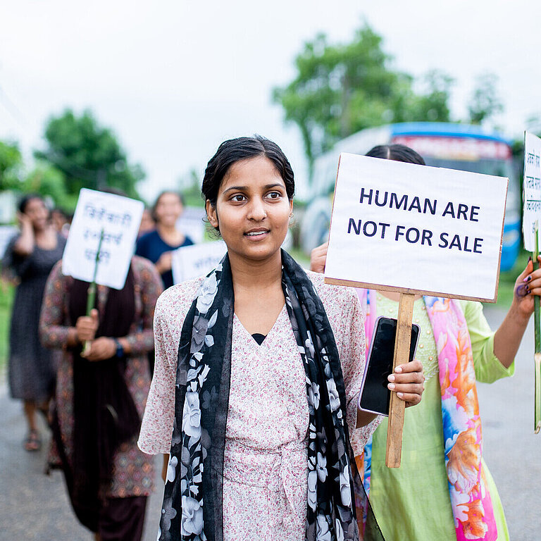 Eine Gruppe von jungen Frauen läuft mit Protestschildern über eine Straße. Auf dem vordersten Schild steht "Humans are not for sale"