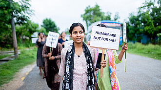 Eine Gruppe von jungen Frauen läuft mit Protestschildern über eine Straße. Auf dem vordersten Schild steht "Humans are not for sale"