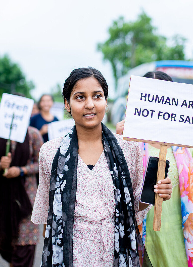 Eine Gruppe von jungen Frauen läuft mit Protestschildern über eine Straße. Auf dem vordersten Schild steht "Humans are not for sale"