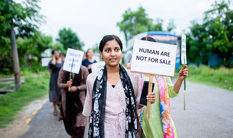 Eine Gruppe von jungen Frauen läuft mit Protestschildern über eine Straße. Auf dem vordersten Schild steht "Humans are not for sale"