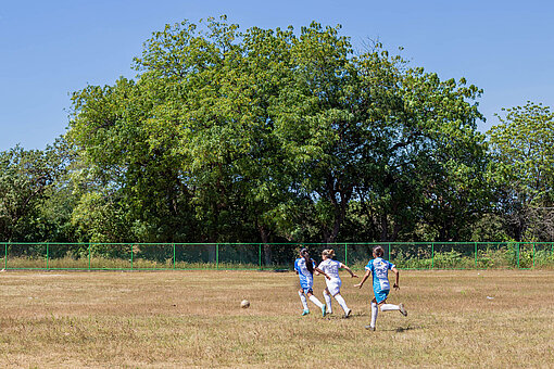 Drei Mädchen rennen auf dem Spielfeld einem Fußall hinterher.